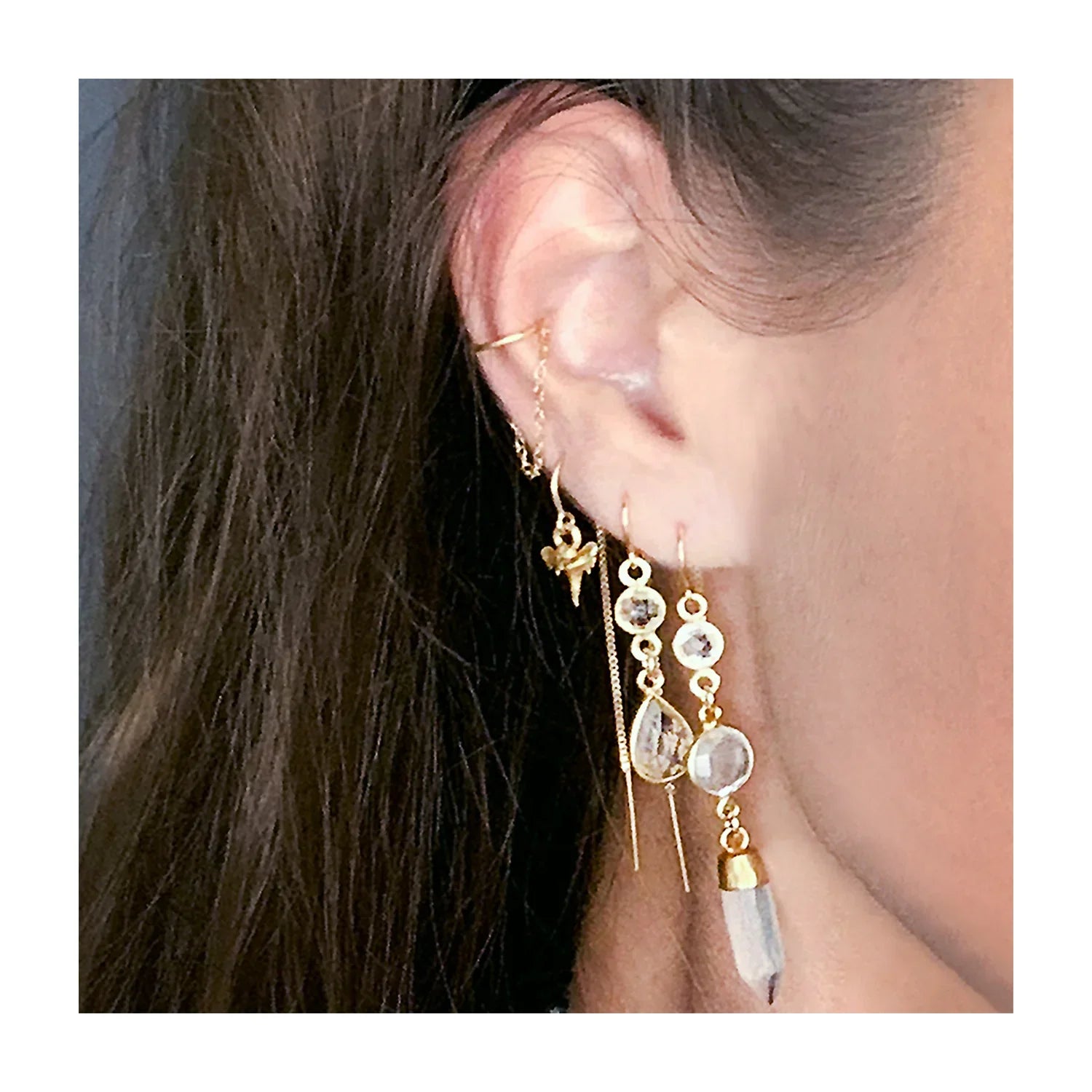 Close-up of an ear wearing gold earrings with dangling beads.